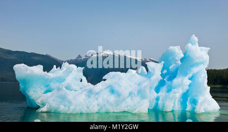 Ein Eisberg und seine Reflexion in Endicott Arm fjord kontrastiert mit dem Himmel, Wasser und Wald der Tongass National Forest in Südostalaska. Stockfoto