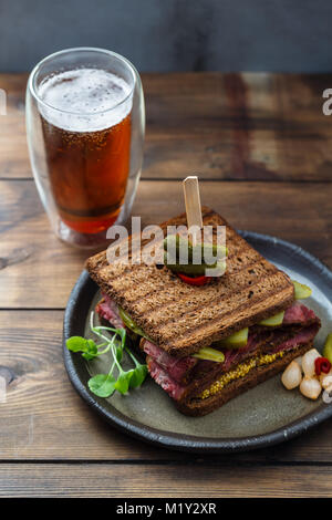 Pastrami Sandwich mit Senf und Gurken mit Bier auf hölzernen Hintergrund Stockfoto