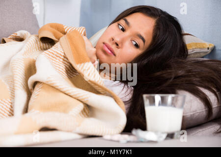 Krankes Mädchen zu Hause am Sofa in der Nähe von Pillen und Glas Milch Stockfoto