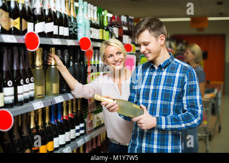 Glückliches junges Paar Auswahl Flasche Champagner im Supermarkt und lächelnd Stockfoto
