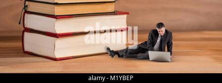 Geschäftsmann mit Computer auf dem Boden neben einem Stapel Bücher Stockfoto