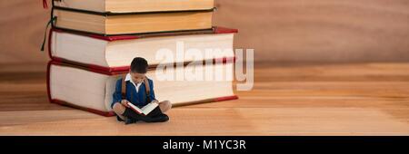 Ein Knabe auf dem Boden neben einem Stapel Bücher Stockfoto