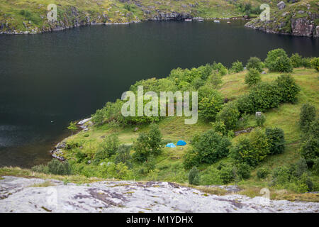 Zwei blaue Zelte auf grünem Gras in der Nähe von einem See. Stockfoto