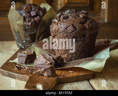 Leckere hausgemachte Schokolade Muffins in braunem Papier auf Holz Schneidebrett. Rustikale Küche Innenraum ländlichen Stil. Quadratisches Format Stockfoto