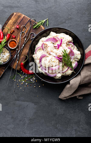 Schaschlik marinierte für Grill in Zwiebeln, Paprika und Gewürzen. Rohes Schweinefleisch für würzige Shish Kebab am Spieß auf schwarzem Hintergrund, Ansicht von oben Stockfoto