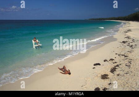 Die Bahamas. Bimini Islands. Karibik Insel. Frau am Strand Relaxen auf Plattform im flachen tropischen Wasser. Mann, Sonnenbaden am Strand. Stockfoto