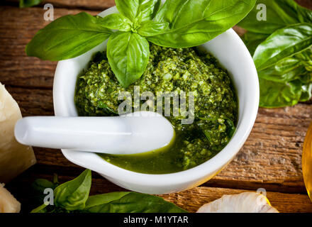 Hausgemachte Pesto mit Basilikum und Pinienkernen in weißem Mörtel über alten Holztisch Stockfoto