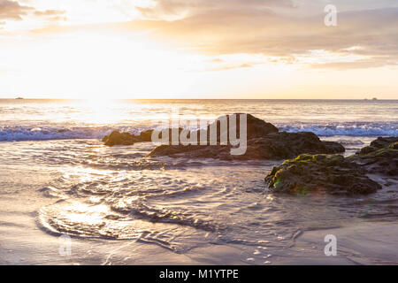 Sonnenuntergang auf die Wellen und nasser Sand mit einer Gruppierung von Felsen in der Unterseite des Rahmens an der Playa Flamingo, Costa Rica Stockfoto