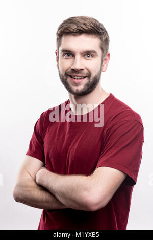 Fröhlicher junger Mann posiert Während verschränkte seine Arme Stockfoto