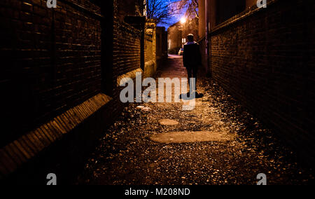 Ein junger Mann allein zu Haus wandern in der Nacht durch eine dunkle Gasse in Großbritannien. Stockfoto