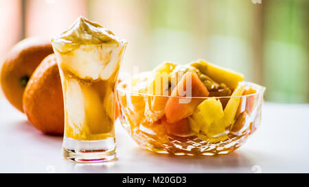 Obstsalat, Joghurt im Glas Schüssel und Orangen, gesundes Frühstück, Seitenansicht, Nahaufnahme. Bunte Frühstück auf weißer Tisch, essen Makro, Orange, Gelb. Stockfoto