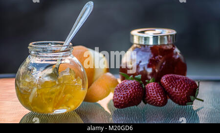 Bunte Marmeladen in Gläsern und organische frisches Obst, Nahaufnahme, Makro essen. Seitenansicht gelb orange Marmelade, frischen Orange, Rot strawberry jam. Stockfoto