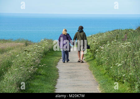 Blaues Meer, Vogelbeobachter (Paar) halten sie Hände, tragen lange objektiv Kameras & gehen Sie weg - Bempton Cliffs RSPB Reservat, East Yorkshire, England Stockfoto