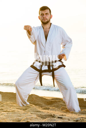 Jungen Kerl üben Karate stellt am Meer in sonniger Morgen im Freien Stockfoto