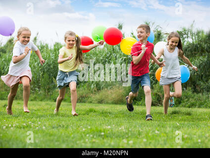 Verspielte Grundschulalter Jungen und Mädchen mit Luftballons und läuft im Sommer Park. Selektiver Fokus Stockfoto