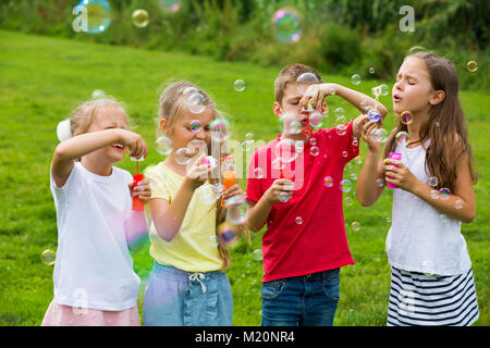 Kinder im Grundschulalter stehen auf grünem Gras und Seifenblasen Stockfoto