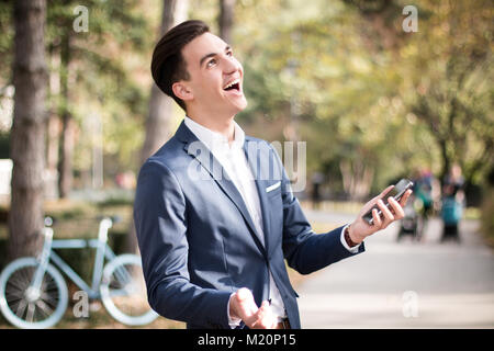 Elegante junge Mann mit Smartphone im Freien in einem Park. Glücklich, fröhlich. Stockfoto