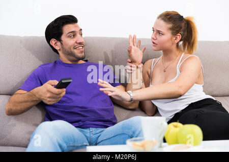 Junge Paare streiten, weil der TV-Fernbedienung auf der Couch sitzen Stockfoto