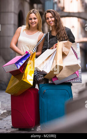 Zwei lächelnde junge Frauen mit Koffern und Taschen auf der Straße stehend Stockfoto