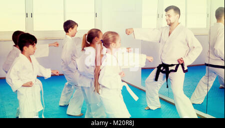 Lächelnde Kinder Karate Tritte mit männlichen Trainer während Karate Klasse Stockfoto