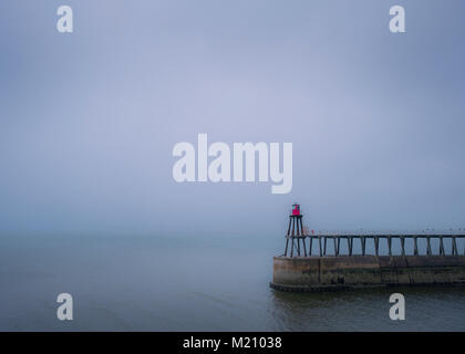 Der Osten Pier und Leuchtturm in Whitby an einem nebligen und verregneten Tag. Stockfoto