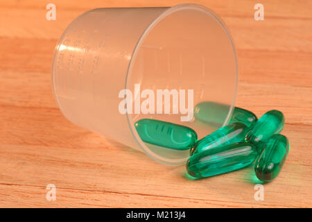 Pillen in Glas umgeworfen und auf einem hölzernen Tisch verstreut. Umgeworfen Pillen - Glas Container und grüne Kapseln an einem hölzernen Tisch. Stockfoto