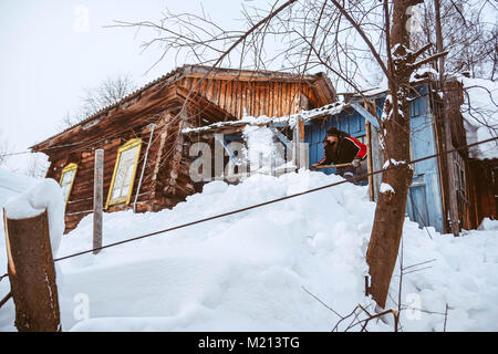 Ein junger Mann wirft eine Schaufel Schnee auf dem Dach der Hütte. Stockfoto