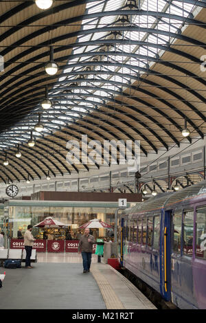 Passagiere warten Zug unter dem langen geschwungenen Dach von Newcastle Central Railway Station, North East England, Großbritannien Stockfoto