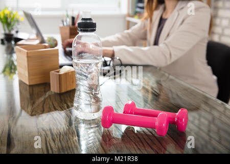 Nahaufnahme einer Geschäftsfrau mit einer Flasche Wasser und Fitness Hanteln auf Büro Schreibtisch Stockfoto