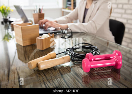 Nahaufnahme einer Geschäftsfrau mit einem Fitness Hanteln und Springseil auf Büro Schreibtisch Stockfoto