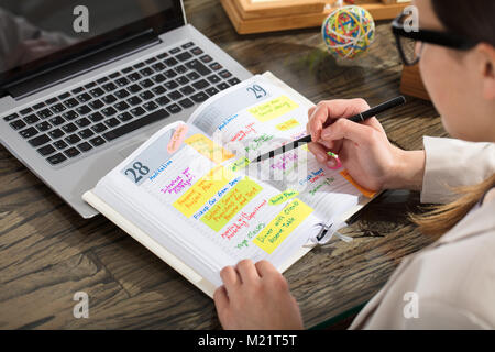 Nahaufnahme der Kaufmann Schreiben Zeitplan im Tagebuch auf hölzernen Schreibtisch Stockfoto