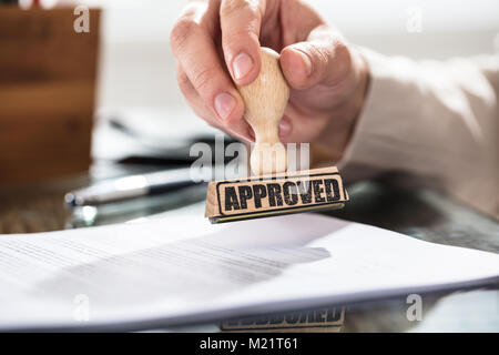 Nahaufnahme einer Person Holding genehmigt Stempel auf Dokument über den Schreibtisch im Büro Stockfoto
