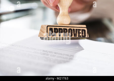 Nahaufnahme einer Person Holding genehmigt Stempel auf Dokument über den Schreibtisch im Büro Stockfoto