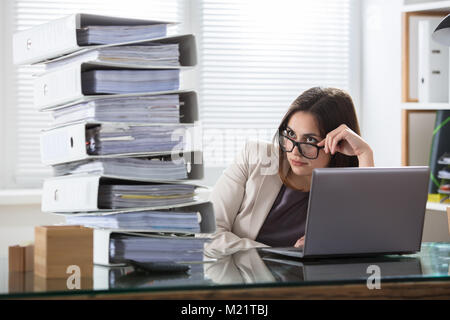Junge besorgt Geschäftsfrau im Stapel von Ordnern auf der Suche auf dem Schreibtisch im Büro Stockfoto