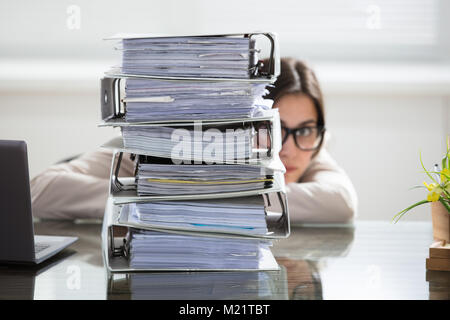 Nahaufnahme einer Geschäftsfrau, die sich hinter den Stapel der Ordner auf dem Schreibtisch am Arbeitsplatz Stockfoto