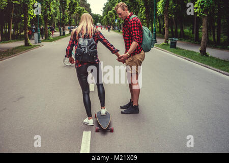 Blonde weibliche learnin Fahrt Longboard mit Casual Male. Stockfoto