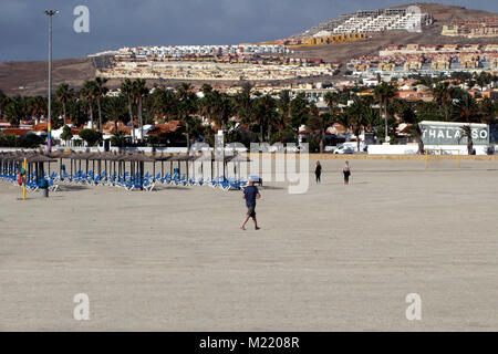 Menschen zu Fuß durch Leere Liegestühle an der Costa Caleta de Fuste Strand auf Fuerteventura auf den Kanarischen Inseln, Spanien, EU. Stockfoto