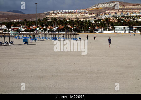 Menschen zu Fuß durch Leere Liegestühle an der Costa Caleta de Fuste Strand auf Fuerteventura auf den Kanarischen Inseln, Spanien, EU. Stockfoto