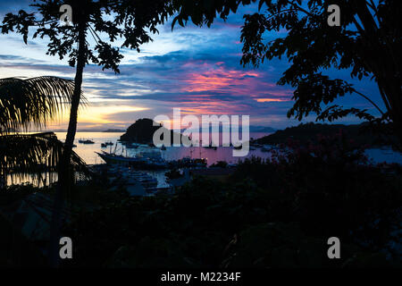 Sonnenuntergang am Hafen von Labuan Bajo mit Booten und Hill und Palmen in den vorderen, Flores, Inonesia Stockfoto