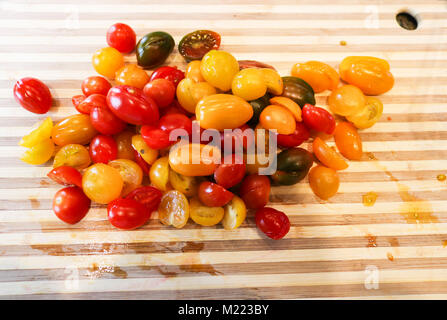 Ein Haufen von saftig bunte Trauben Tomaten in der Hälfte auf einem stiped Holz Schneidebrett bereit zu Gericht, gehackt Stockfoto