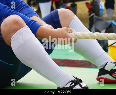 Mann in Blau Sport Outfit im Tauziehen Sport teilnehmen. Schwerpunkt auf seine Hände mit Sand auf ihnen, während der Vorbereitung zu beginnen, Ziehen, Seil, die versuchen, h Stockfoto