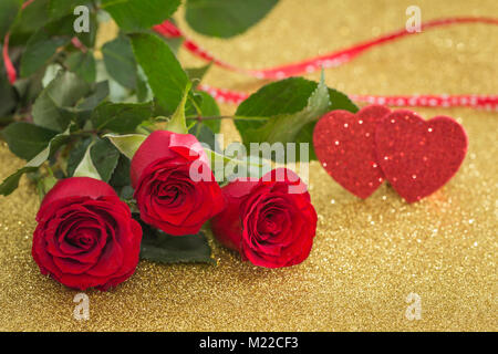 Wunderschöne rote Rosen mit dekorativer Herzen auf einen goldenen Hintergrund Stockfoto