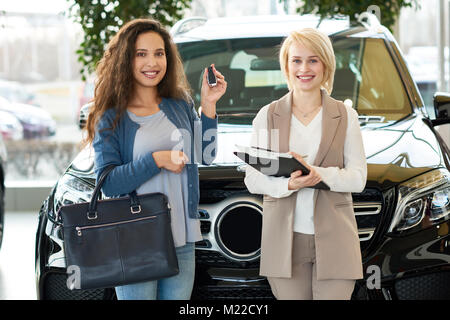 Group Portrait von fröhlichen curly Kunden, Gedrückthalten der Taste und Blonde Verkäuferin mit Klemmbrett in der Hand neben ihr und posieren für Fotografie af Stockfoto