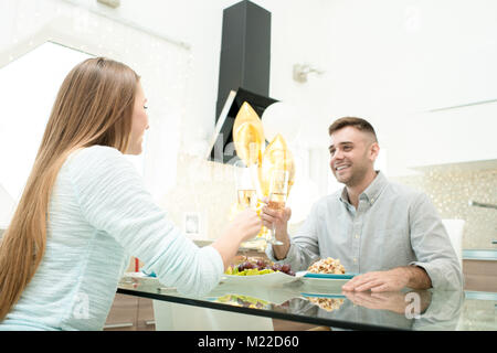 Portrait von glückliches junges Paar Diner zusammen in der modernen Küche und klirren Gläser Champagner Glas sitzen am Tisch Stockfoto