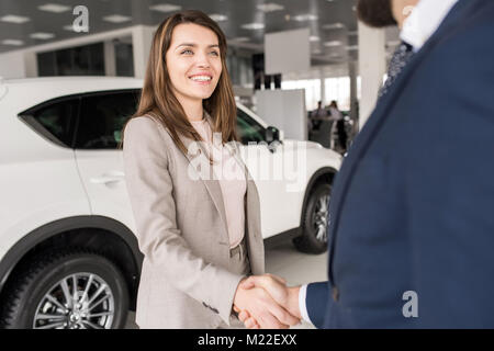 Portrait von glücklichen jungen Frau die Hände schütteln mit dem Auto Verkäufer nach dem Kauf neuer Luxus Auto Dealership showroom Stockfoto
