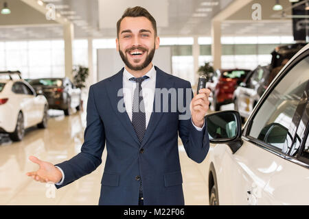 Portrait von stattlichen Autoverkäufer ein Holding Autoschlüssel und freundlich lächelnd an Kamera stehend in Luxus dealership Showroom Stockfoto
