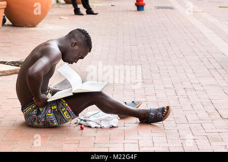 Cartagena, Kolumbien - Januar 23th, 2018: Ein junger afro-amerikanische kolumbianischen Mann sitzt auf der Straße, auf den weißen Seiten eines Notebooks auf der Plaza Stockfoto