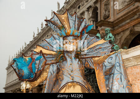 Karneval in Venedig - Weibliche Venezianische Maske in bunten und eleganten Kostüm auf dem Markusplatz in Venedig mit traditionellen venezianischen Architektur Stockfoto