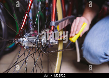 Thema Reparatur Fahrräder. Nahaufnahme der Hand eines kaukasischen Mann einem Kettenschmierstoff in einem gelben Öler für llubricator ein Fahrrad Kette auf ein rotes Fahrrad. Stockfoto