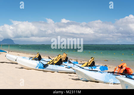 Blau und Weiß Kajaks mit Schwimmwesten auf sandigen Strand von Mauritius, sonniger Tag mit Wolken im Himmel und die Berge im Hintergrund. Stockfoto